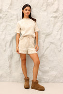 Woman wearing a beige outfit with brown boots against a textured white background