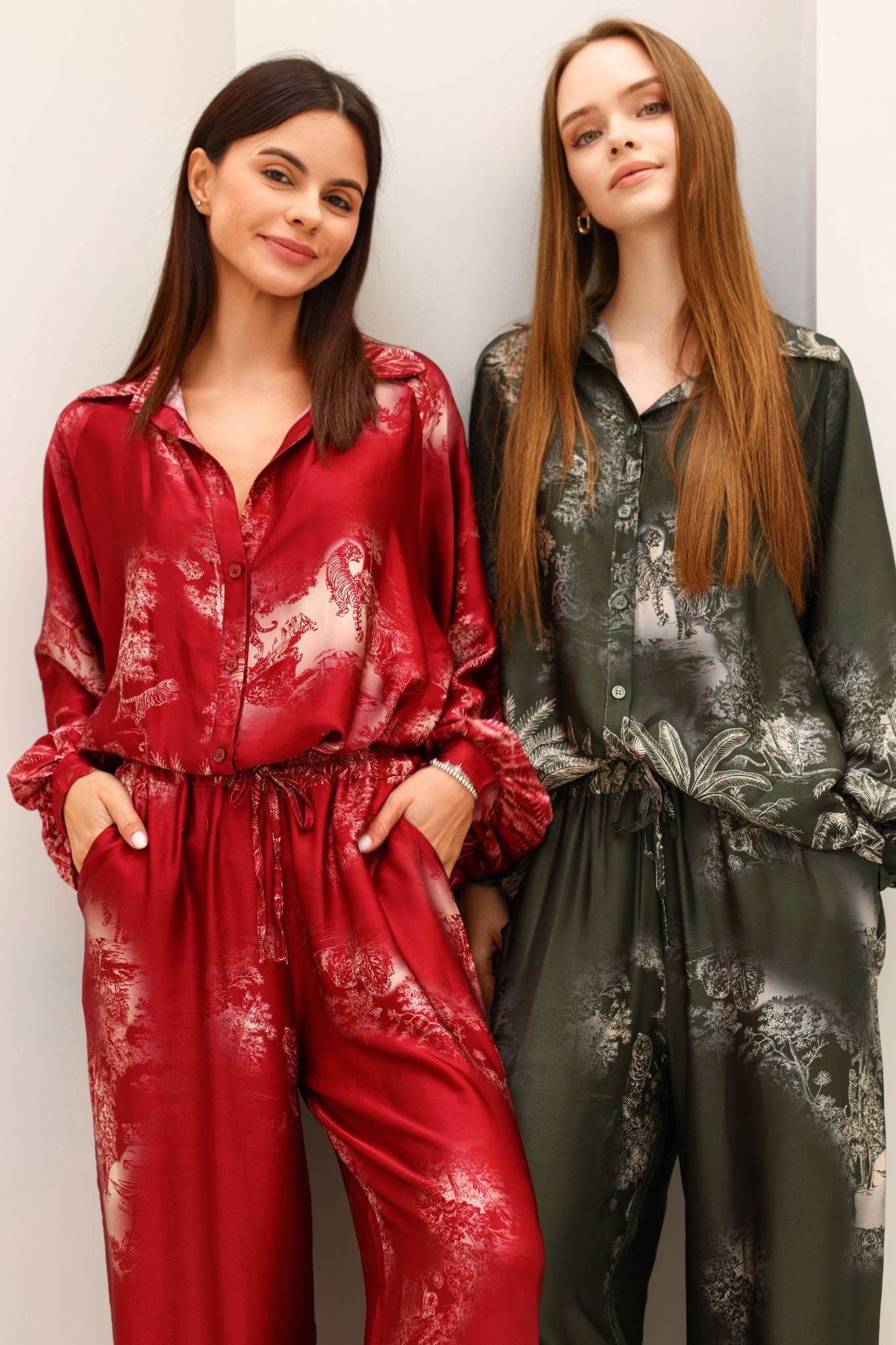 Two women wearing floral-patterned jumpsuits against a plain background