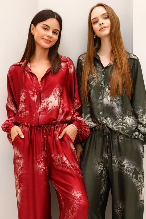 Two women wearing floral-patterned jumpsuits against a plain background