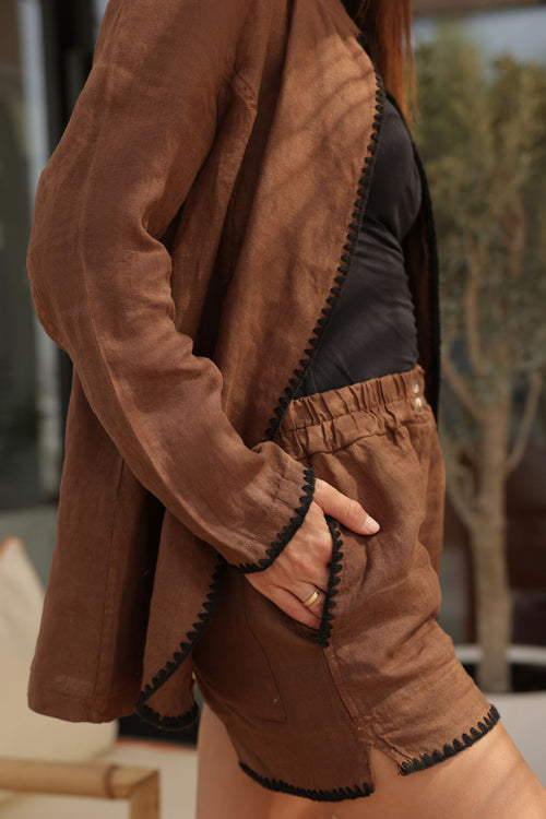 Person wearing a brown linen jacket and shorts with black trim outdoors.