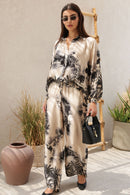 Woman wearing a floral outfit standing  outdoors with plants and a black handbag