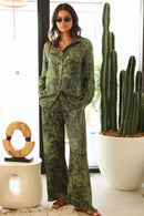 Woman in green patterned outfit standing next to a potted cactus indoors.