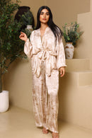 Woman in a patterned robe standing in a room with plants and stairs.