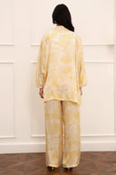 Person wearing a yellow floral outfit standing against a white paneled wall.