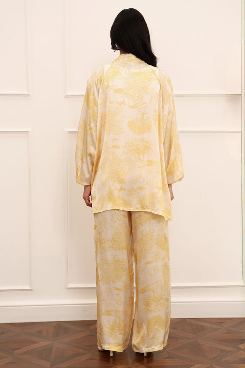 Person wearing a yellow floral outfit standing against a white paneled wall.