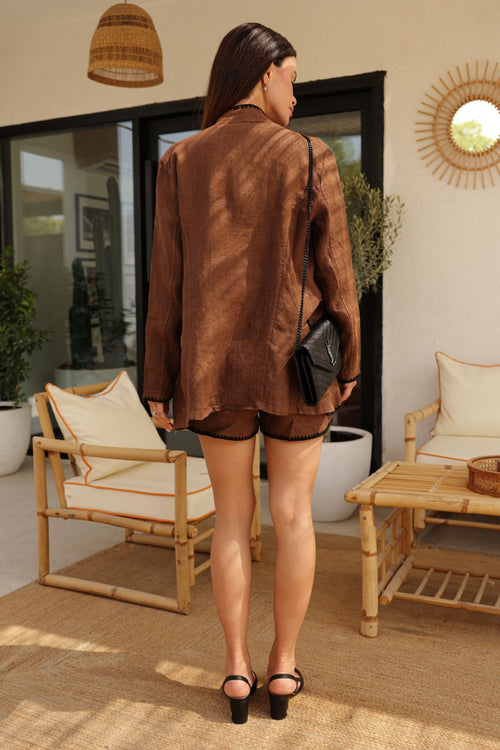 Woman in a brown jacket and shorts standing in a modern living room.