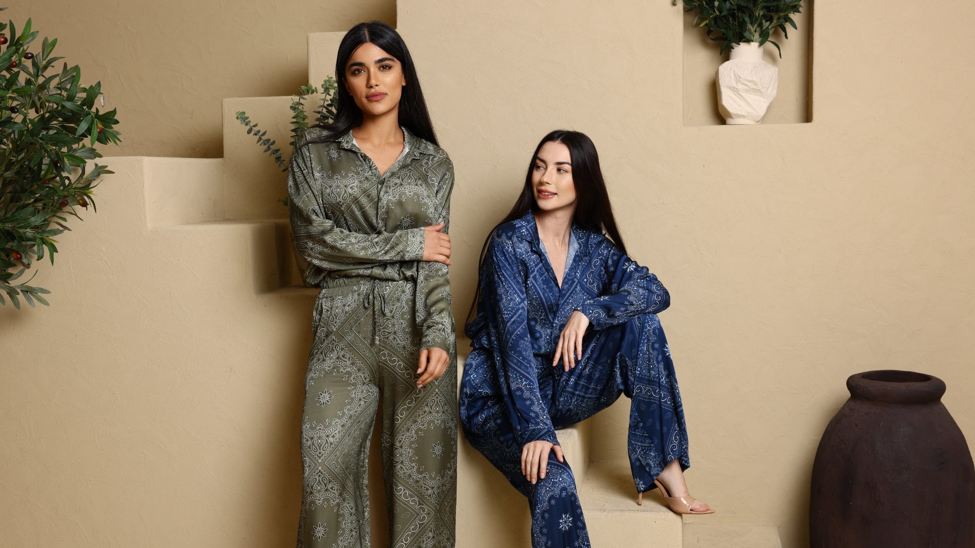 Two women in patterned outfits sitting on a beige couch with a neutral background